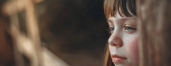 little girl standing by a wooden fence staring 